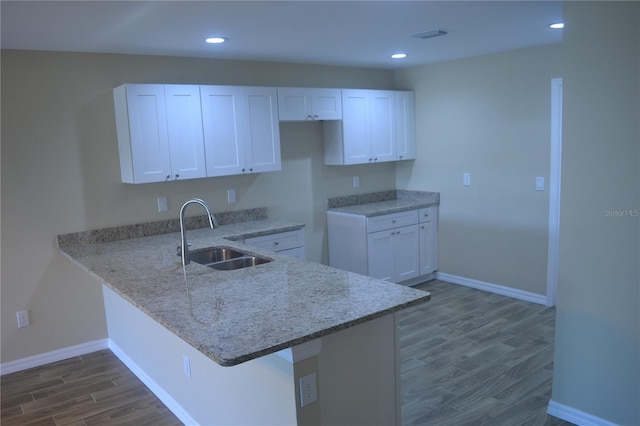 kitchen with white cabinets, kitchen peninsula, light stone counters, and sink