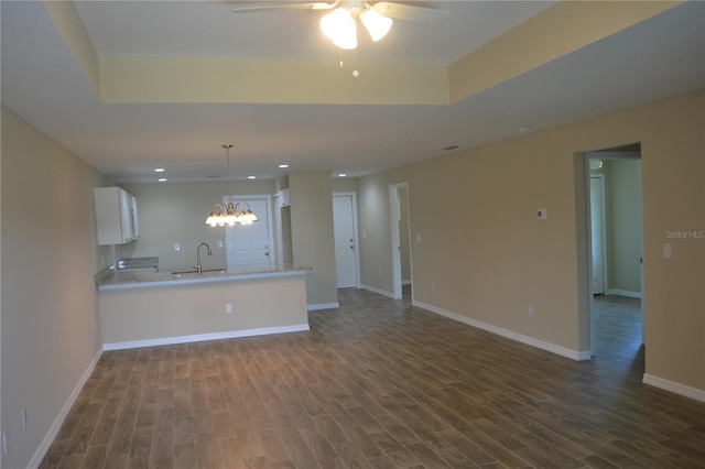 unfurnished living room with a tray ceiling, dark hardwood / wood-style floors, ceiling fan with notable chandelier, and sink