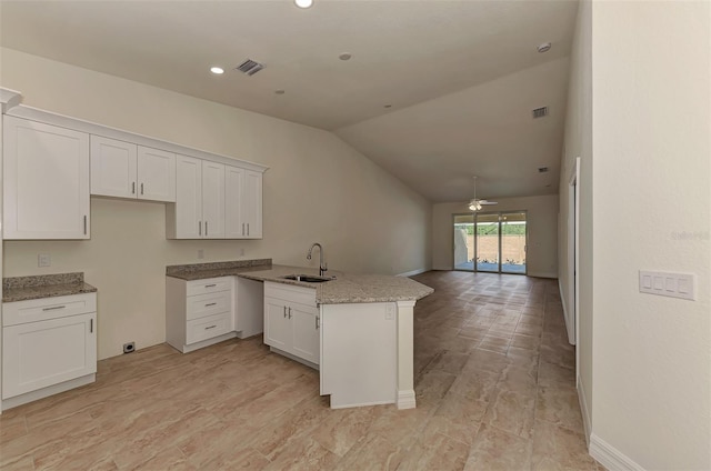 kitchen featuring ceiling fan, sink, white cabinets, vaulted ceiling, and light stone countertops