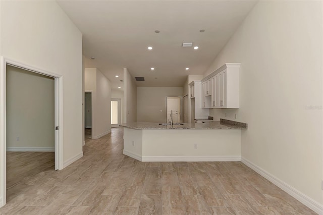 kitchen with white cabinets, kitchen peninsula, light stone countertops, and sink