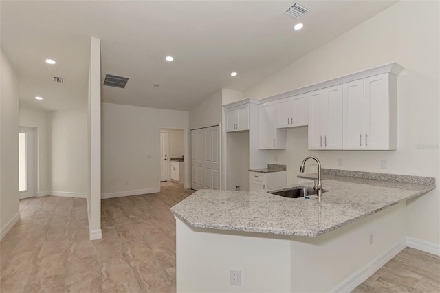 kitchen with lofted ceiling, kitchen peninsula, sink, white cabinets, and light stone counters