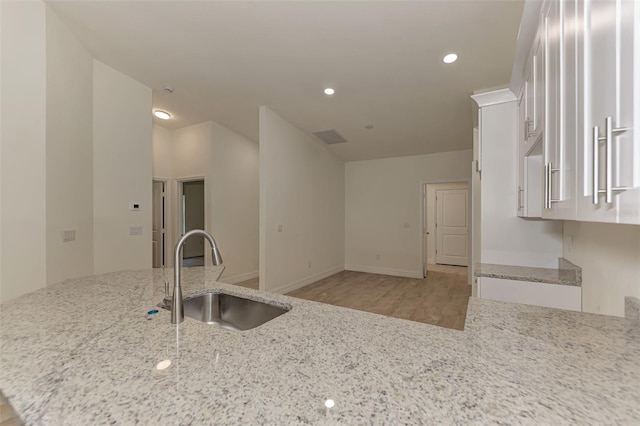 kitchen with light stone countertops, kitchen peninsula, light wood-type flooring, and sink