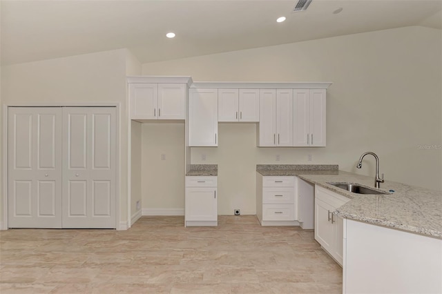 kitchen featuring light stone counters, white cabinetry, sink, and lofted ceiling