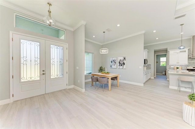 foyer entrance with an inviting chandelier, crown molding, light hardwood / wood-style floors, and french doors