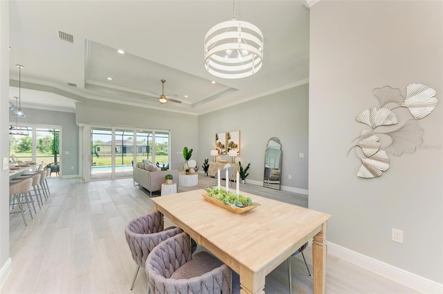 dining room featuring light hardwood / wood-style floors, ceiling fan with notable chandelier, a tray ceiling, and a wealth of natural light