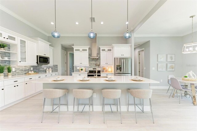 kitchen with appliances with stainless steel finishes, backsplash, wall chimney exhaust hood, and a center island with sink