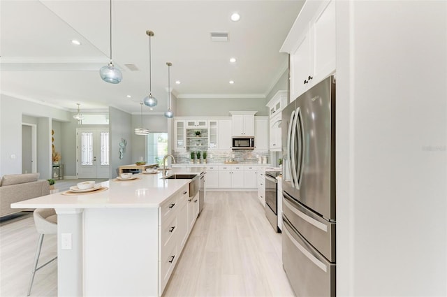 kitchen with a breakfast bar area, stainless steel appliances, white cabinets, and a kitchen island with sink