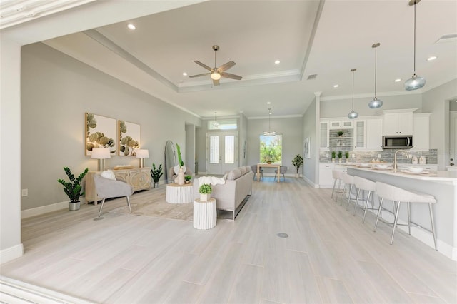 living room featuring ceiling fan, a raised ceiling, sink, and ornamental molding