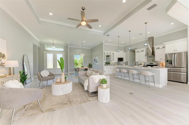 living room featuring crown molding, a raised ceiling, french doors, and ceiling fan with notable chandelier