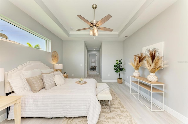 bedroom with light hardwood / wood-style floors, ceiling fan, and a tray ceiling