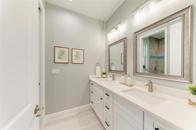 bathroom featuring large vanity, double sink, and a tile shower