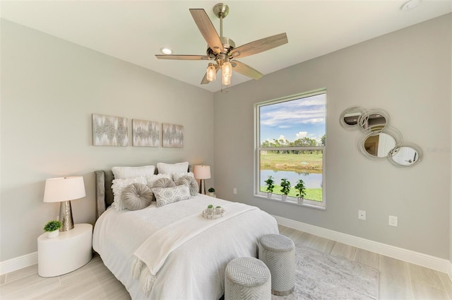 bedroom featuring light hardwood / wood-style flooring, ceiling fan, and a water view