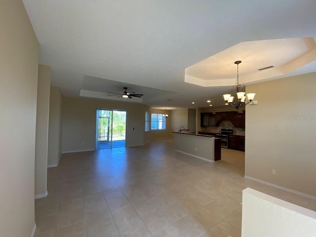 tiled empty room with a tray ceiling and ceiling fan with notable chandelier