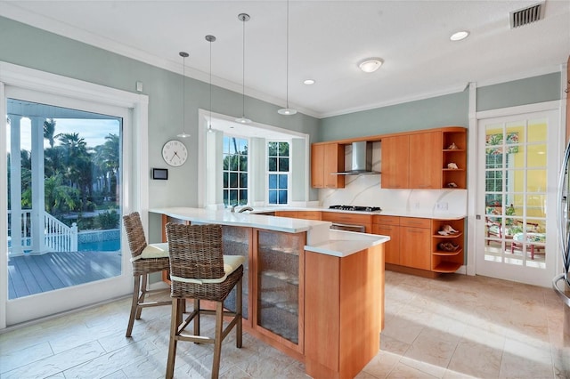 kitchen with white gas stovetop, wall chimney exhaust hood, decorative light fixtures, a kitchen bar, and kitchen peninsula