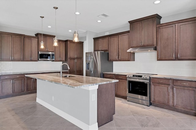 kitchen featuring appliances with stainless steel finishes, sink, backsplash, a center island with sink, and light stone countertops