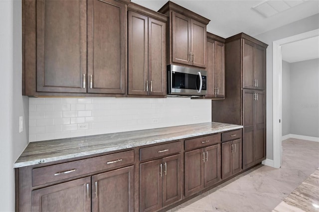 kitchen with backsplash, dark brown cabinets, light tile floors, and light stone counters