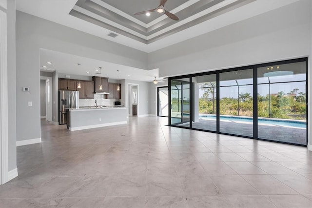 unfurnished living room with a tray ceiling, a towering ceiling, sink, light tile floors, and ceiling fan