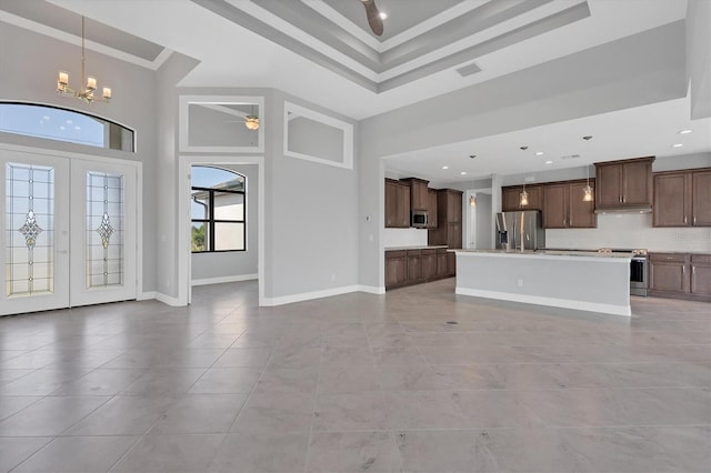 unfurnished living room with crown molding, a towering ceiling, light tile floors, and a tray ceiling