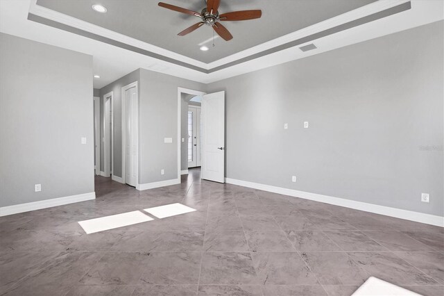 tiled empty room featuring a raised ceiling and ceiling fan