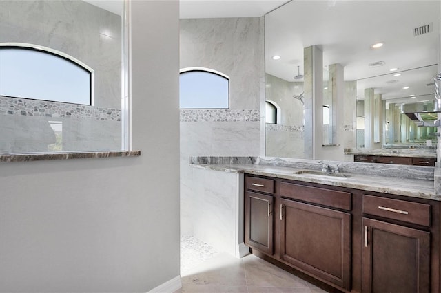 bathroom featuring tile flooring, vanity, a tile shower, and tile walls