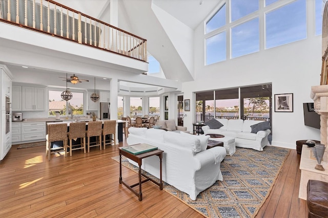 living room with a wealth of natural light, light hardwood / wood-style flooring, high vaulted ceiling, and ceiling fan