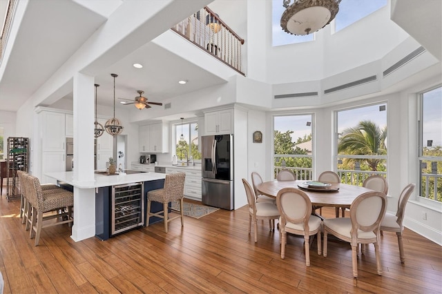 dining room with sink, light hardwood / wood-style flooring, ceiling fan, a towering ceiling, and beverage cooler