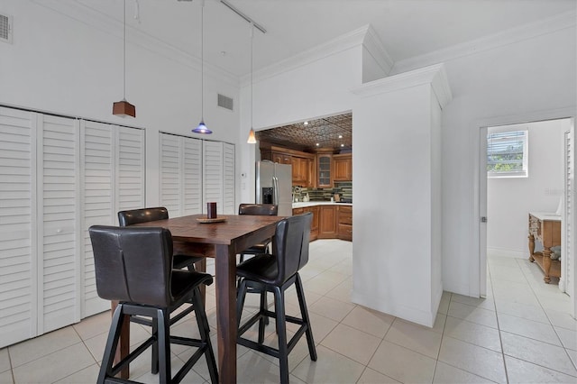 dining area featuring a high ceiling, rail lighting, light tile patterned floors, and ornamental molding