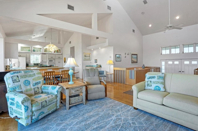 living room featuring wood-type flooring, ceiling fan with notable chandelier, and high vaulted ceiling