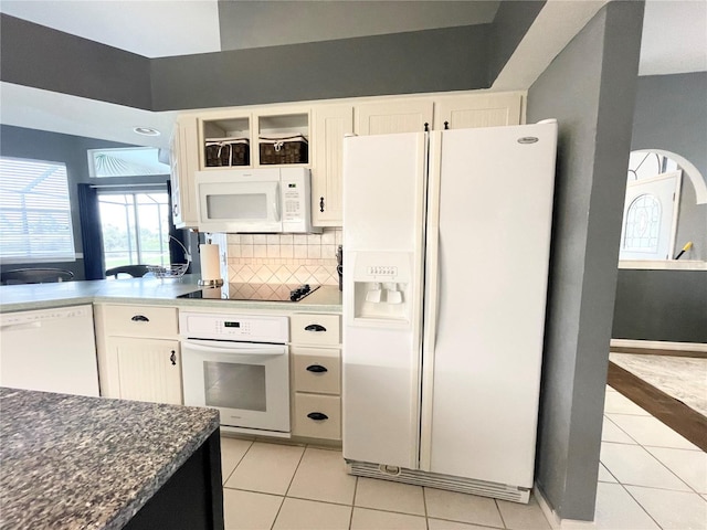 kitchen featuring white appliances, dark stone countertops, light tile patterned floors, tasteful backsplash, and white cabinetry