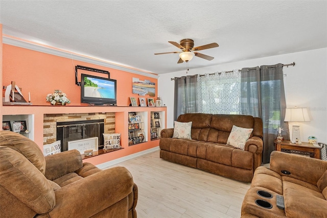 living room featuring ceiling fan, a stone fireplace, light hardwood / wood-style floors, and a textured ceiling