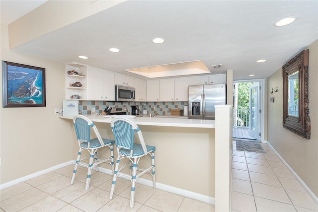 kitchen featuring kitchen peninsula, appliances with stainless steel finishes, a kitchen bar, tasteful backsplash, and white cabinetry