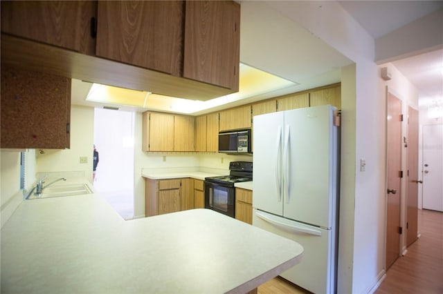 kitchen featuring black appliances, light hardwood / wood-style floors, kitchen peninsula, and sink