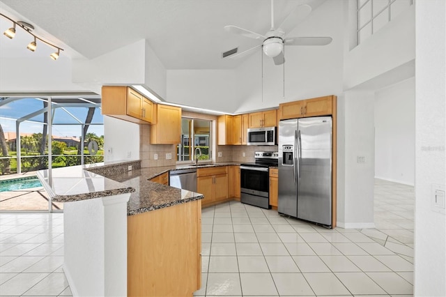 kitchen featuring kitchen peninsula, dark stone countertops, decorative backsplash, light tile patterned floors, and appliances with stainless steel finishes