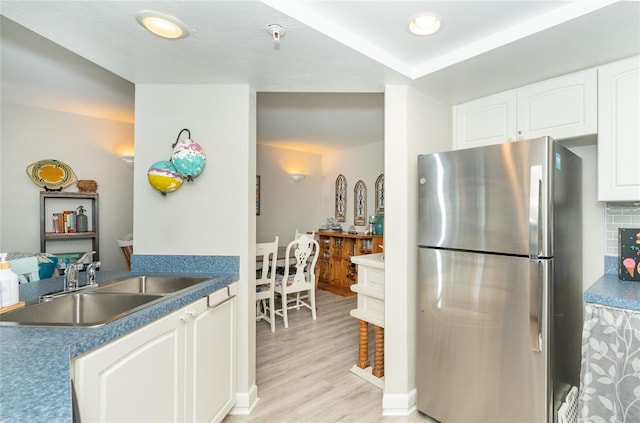 kitchen featuring sink, light hardwood / wood-style flooring, decorative backsplash, stainless steel fridge, and white cabinetry