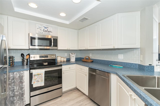 kitchen with white cabinets, appliances with stainless steel finishes, and a tray ceiling