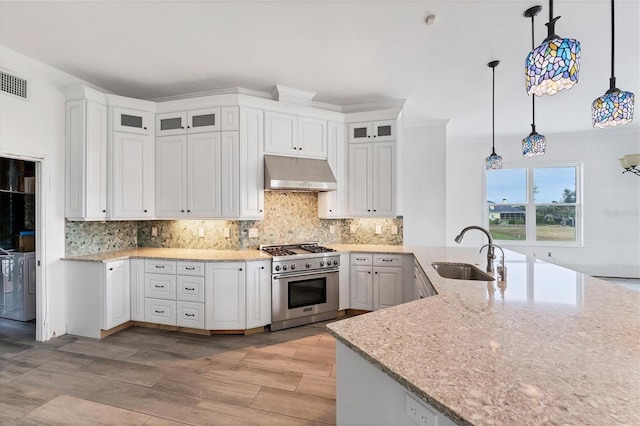 kitchen featuring high end stainless steel range, sink, ventilation hood, pendant lighting, and white cabinets