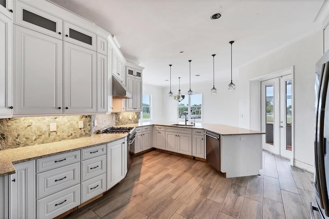 kitchen with appliances with stainless steel finishes, sink, backsplash, light hardwood / wood-style floors, and pendant lighting