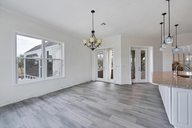 unfurnished dining area featuring a notable chandelier, french doors, sink, and light wood-type flooring