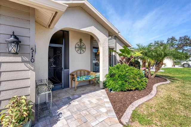 entrance to property featuring a lawn and a patio