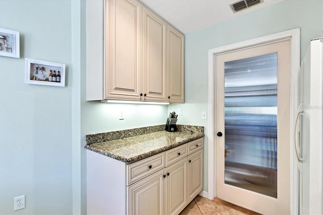 kitchen with dark stone countertops, cream cabinetry, and light tile flooring