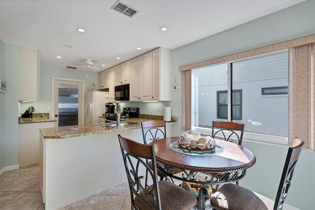 kitchen featuring light tile flooring, stone counters, white fridge, and ceiling fan