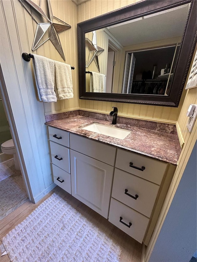 bathroom featuring vanity, hardwood / wood-style flooring, toilet, and wood walls