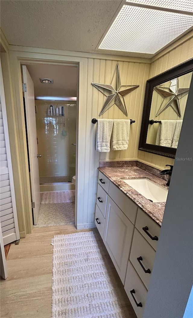 bathroom with wooden walls, hardwood / wood-style flooring, vanity, walk in shower, and a textured ceiling