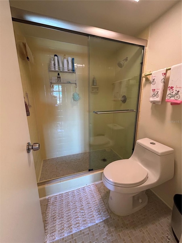 bathroom with tile patterned floors, toilet, and a shower with door