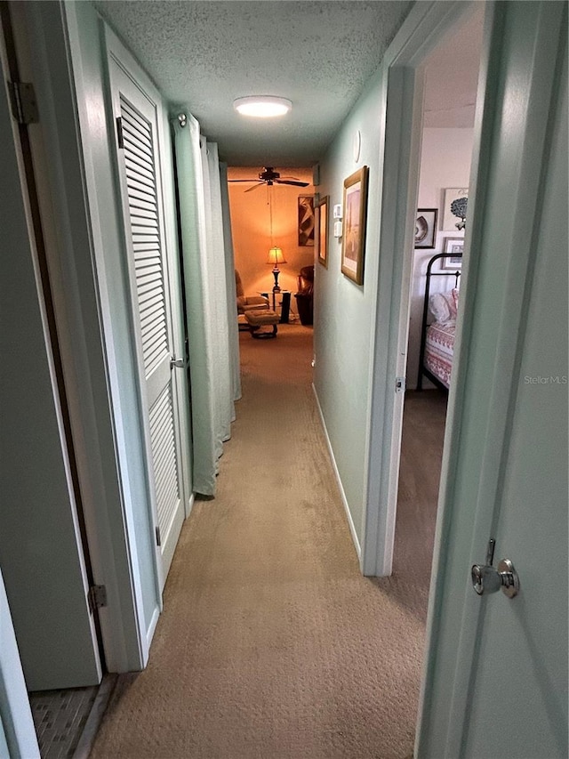 hallway with light carpet and a textured ceiling