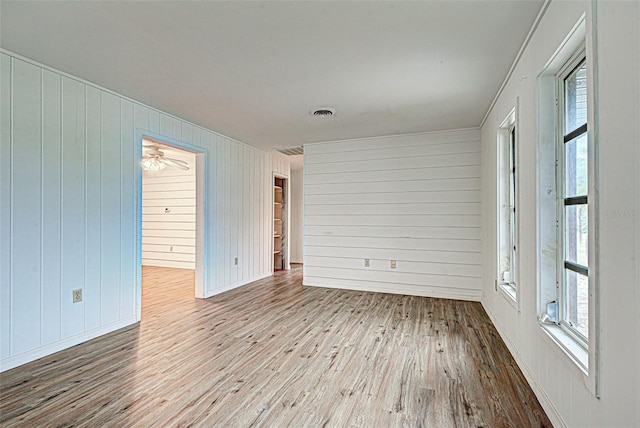 empty room featuring wooden walls, light hardwood / wood-style floors, and ceiling fan