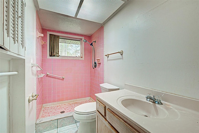 bathroom with tile floors, toilet, a tile shower, and vanity