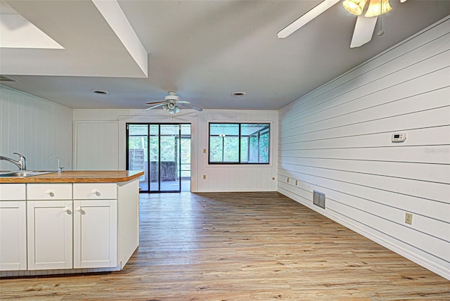 kitchen featuring ceiling fan, sink, white cabinets, wood walls, and light wood-type flooring