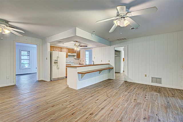 kitchen featuring light hardwood / wood-style floors, ceiling fan, kitchen peninsula, white fridge with ice dispenser, and tasteful backsplash