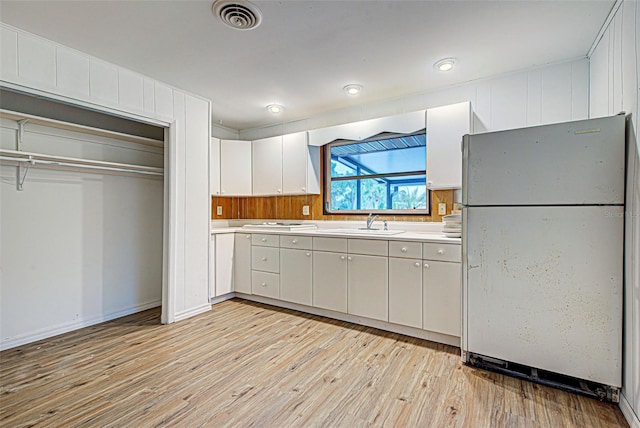 kitchen with light hardwood / wood-style flooring, stainless steel refrigerator, white cabinetry, and sink